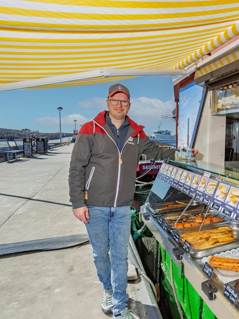 Tobias Krüger an der Imbiss-Theke mit Räucherfisch-Auslage und Hafenblick